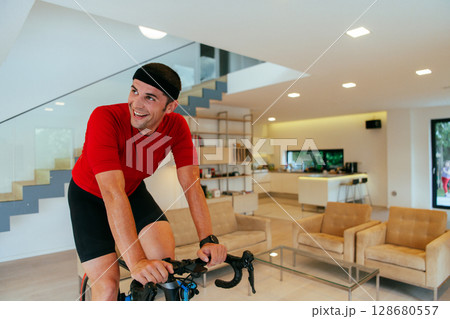A triathlete riding a triathlon bike on a machine simulation in a modern living room A triathlete riding a triathlon bike on a machine simulation in a modern living room 128680557