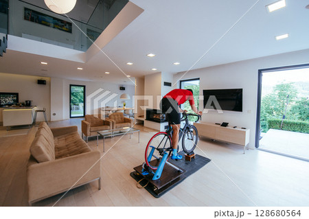 A triathlete riding a triathlon bike on a machine simulation in a modern living room A triathlete riding a triathlon bike on a machine simulation in a modern living room 128680564