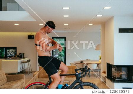 A triathlete riding a triathlon bike on a machine simulation in a modern living room A triathlete riding a triathlon bike on a machine simulation in a modern living room 128680572