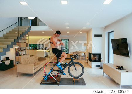 A triathlete riding a triathlon bike on a machine simulation in a modern living room 128680586