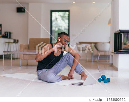 Training At Home. Sporty man doing the training while watching an online tutorial on a laptop, exercising in the living room, free space. Training At Home. Sporty man doing the training while watching an online tutorial on a laptop, exercising in the living room, free space. 128680622