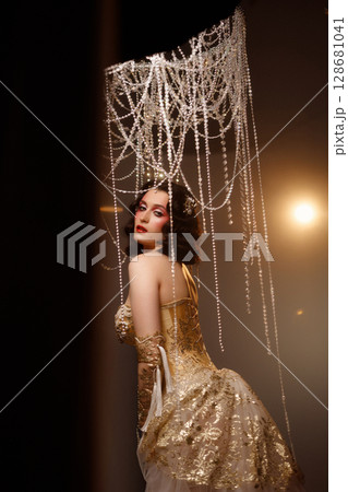 Retro-style performer in vintage costume posing on dark stage under chandelier 128681041