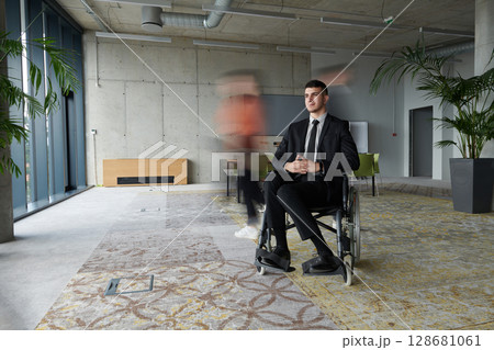 A businessman in a wheelchair navigating through a busy office, surrounded by his colleagues who are actively engaged in their work and collaboration 128681061