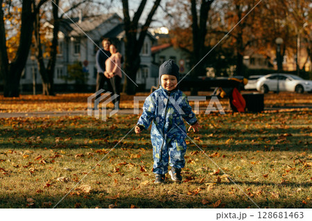 A joyful little boy in his winter coat and hat plays happily in the park, surrounded by the love and warmth of his smiling parents A joyful little boy in his winter coat and hat plays happily in the park, surrounded by the love and warmth of his smiling parents 128681463