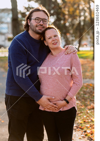 A man lovingly embraces his pregnant wife in the park, sharing a peaceful moment of warmth and affection A man lovingly embraces his pregnant wife in the park, sharing a peaceful moment of warmth and affection 128681469