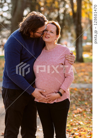 A man lovingly embraces his pregnant wife in the park, sharing a peaceful moment of warmth and affection  128681470