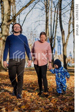 A loving couple strolls through a sunlit park with their young son, surrounded by the vibrant colors of autumn, enjoying a joyful and peaceful family moment together. 128681502