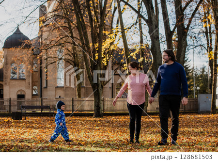 A loving couple strolls through a sunlit park with their young son, surrounded by the vibrant colors of autumn, enjoying a joyful and peaceful family moment together. 128681503