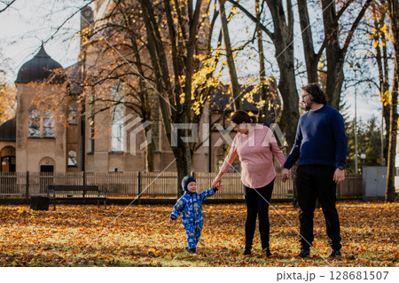 A loving couple strolls through a sunlit park with their young son, surrounded by the vibrant colors of autumn, enjoying a joyful and peaceful family moment together. 128681507