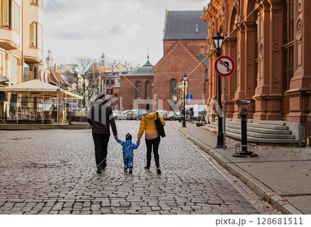 Parents walking hand in hand with their son through the charming city streets, enjoying the warmth of the season and creating joyful memories together Parents walking hand in hand with their son through the charming city streets, enjoying the warmth of the season and creating joyful memories together 128681511