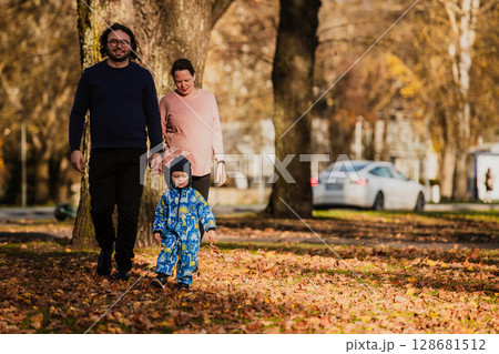 A loving couple strolls through a sunlit park with their young son, surrounded by the vibrant colors of autumn, enjoying a joyful and peaceful family moment together. 128681512