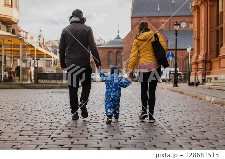 Parents walking hand in hand with their son through the charming city streets, enjoying the warmth of the season and creating joyful memories together Parents walking hand in hand with their son through the charming city streets, enjoying the warmth of the season and creating joyful memories together 128681513