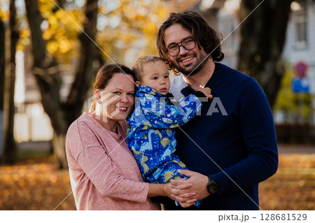 On a sunny autumn day in the park, a mother and father lovingly embrace their young son, sharing moments of laughter and joy as they play together On a sunny autumn day in the park, a mother and father lovingly embrace their young son, sharing moments of laughter and joy as they play together 128681529