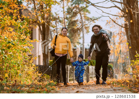 A loving couple strolls through a sunlit park with their young son, surrounded by the vibrant colors of autumn, enjoying a joyful and peaceful family moment together. 128681538