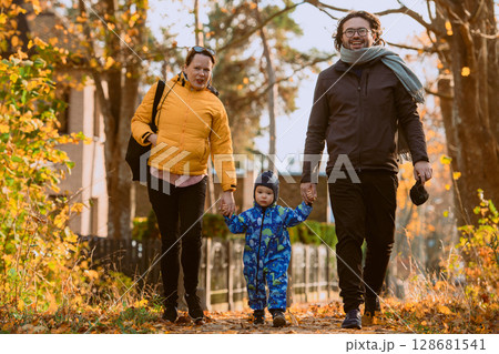 A loving couple strolls through a sunlit park with their young son, surrounded by the vibrant colors of autumn, enjoying a joyful and peaceful family moment together. 128681541