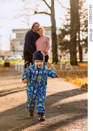 A joyful little boy in his winter coat and hat plays happily in the park, surrounded by the love and warmth of his smiling parents 128681542