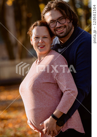 A man lovingly embraces his pregnant wife in the park, sharing a peaceful moment of warmth and affection A man lovingly embraces his pregnant wife in the park, sharing a peaceful moment of warmth and affection 128681564