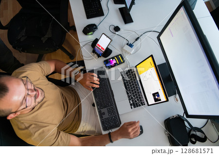 Top view of programmer diligently testing smartphone applications while sitting in their office. Top view of programmer diligently testing smartphone applications while sitting in their office. 128681571