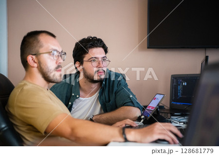 Programmers engrossed in deep collaboration, diligently working together to solve complex problems and develop innovative mobile applications with seamless functionality. 128681779