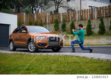 A man meticulously washes and cleans his car in the driveway of his home, showcasing pride in his vehicle and outdoor space. A man meticulously washes and cleans his car in the driveway of his home, showcasing pride in his vehicle and outdoor space. 128681923