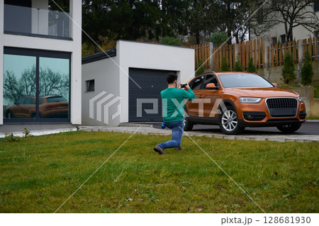 A man meticulously washes and cleans his car in the driveway of his home, showcasing pride in his vehicle and outdoor space. A man meticulously washes and cleans his car in the driveway of his home, showcasing pride in his vehicle and outdoor space. 128681930