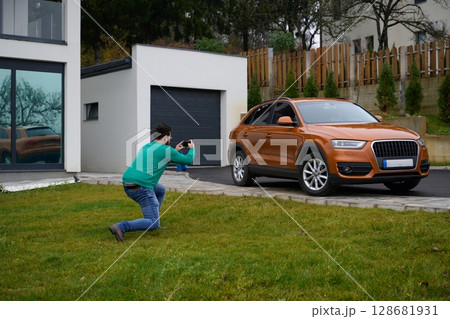A man meticulously washes and cleans his car in the driveway of his home, showcasing pride in his vehicle and outdoor space. A man meticulously washes and cleans his car in the driveway of his home, showcasing pride in his vehicle and outdoor space. 128681931