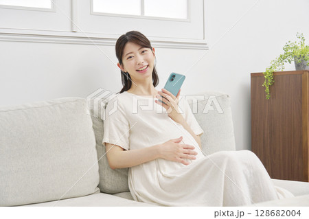 リビングでスマートフォンを持つ妊婦のポートレート 128682004