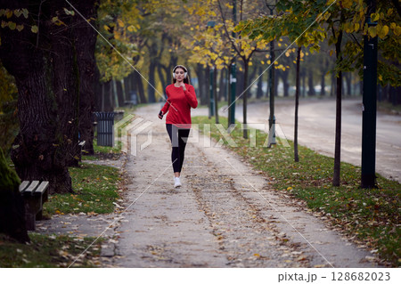 Young beautiful woman running in autumn park and listening to music with headphones on smartphone Young beautiful woman running in autumn park and listening to music with headphones on smartphone 128682023