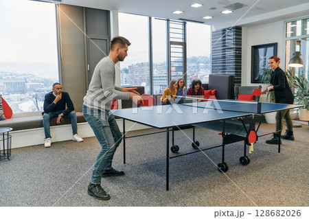 Business colleagues take a break from work to enjoy a game of table tennis, fostering teamwork and camaraderie in the workplace 128682026