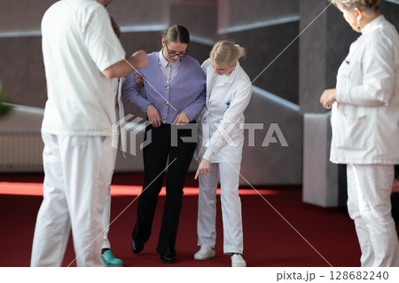 Medical team helping patient with walking therapy 128682240