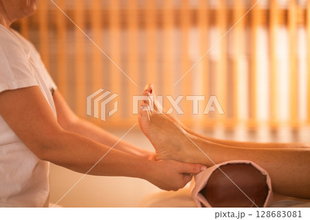 Foot Massage Therapy in a Relaxing Spa Setting. A professional massage therapist in a white uniform provides a soothing foot massage to a client in a calm and serene spa environment 128683081