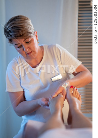 Foot Massage Therapy in a Relaxing Spa Setting. A professional massage therapist in a white uniform provides a soothing foot massage to a client in a calm and serene spa environment 128683084