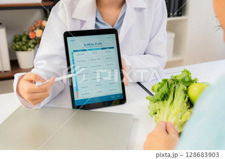 Asian nutritionist using tablet to explaining personalized meal plan with AI to patient. Asian nutritionist using tablet to explaining personalized meal plan with AI to patient. 128683903