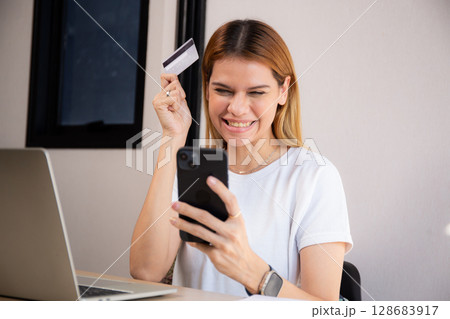 Happy young caucasian woman holding credit card or debit card paying with shopping online. 128683917