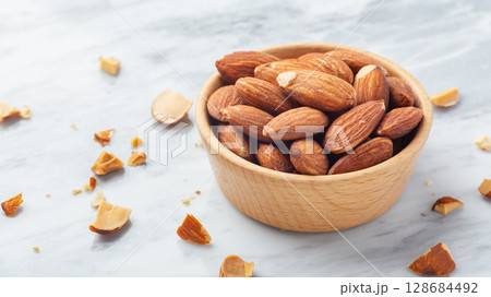 Almond nuts in wood bowl with broken almonds on marble table background 128684492