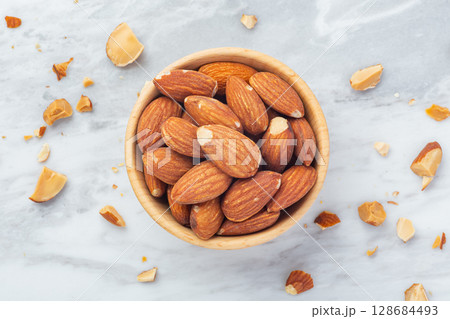 Almond in wooden bowl with broken almonds on marble table background 128684493