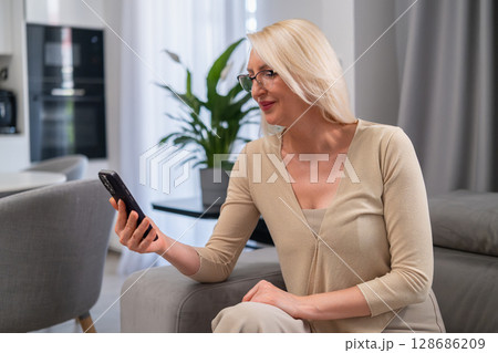 Happy woman holding smartphone, engaged in conversation or browsing. Modern lifestyle, communication, and technology concept. Happy woman holding smartphone, engaged in conversation or browsing. Modern lifestyle, communication, and technology concept. 128686209