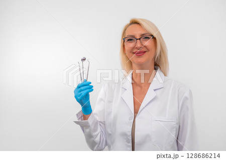 Portrait of confident female dentist with gloves and instruments, ready for dental procedure. Healthcare, clinic and professional care concept 128686214