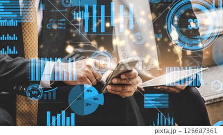 Business professionals analyzing digital data charts and graphs on mobile devices in a modern office environment with overlay graphics and statistics xenic 128687361