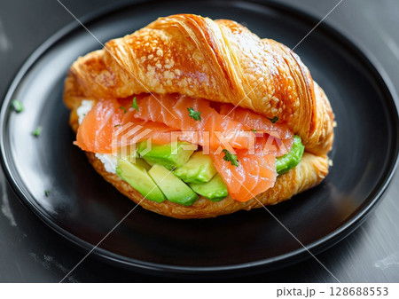 Croissant salmon sandwich with creamy cheese and and fresh avocado on black plate.AI Generative. 128688553