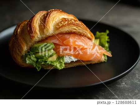 Croissant salmon sandwich with creamy cheese and and fresh avocado on black plate.AI Generative. 128688611