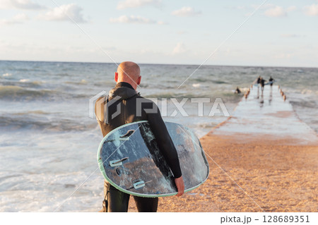 Sportsman with surfboard going to ride waves Sportsman with surfboard going to ride waves 128689351