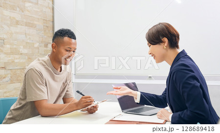 書類にサインするする黒人男性と日本人女性スタッフ 128689418