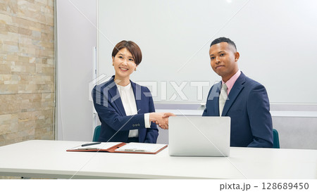ホワイトボードの前で握手する黒人男性ビジネスマンと日本人女性スタッフ 128689450