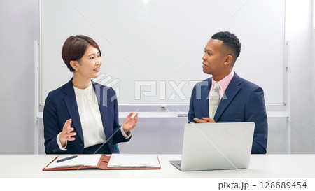 黒人男性ビジネスマンと面談する日本人女性スタッフ 黒人男性ビジネスマンと面談する日本人女性スタッフ 128689454
