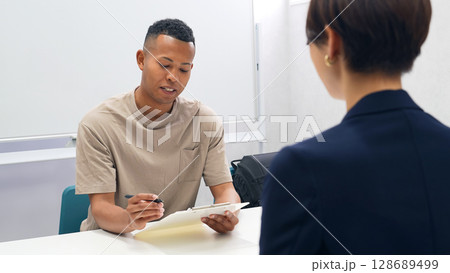 書類にサインするする黒人男性と日本人女性スタッフ 128689499