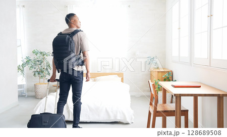 ホテルの部屋にスーツケースを持って立つ黒人男性旅行者 ホテルの部屋にスーツケースを持って立つ黒人男性旅行者 128689508