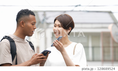 スマホの翻訳アプリを使って黒人男性と会話する日本人女性 スマホの翻訳アプリを使って黒人男性と会話する日本人女性 128689524