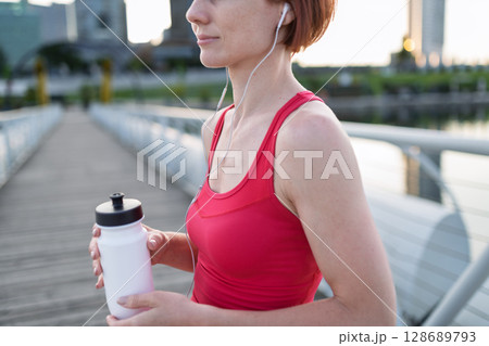 Woman resting after her morning workout, drinking water on a city bridge 128689793