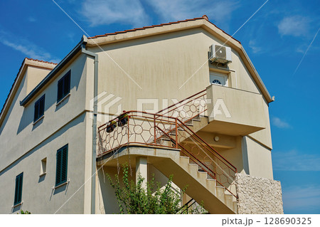Traditional Mediterranean house with stone walls and green shutters against blue sky. Traditional residential architecture in coastal town Traditional Mediterranean house with stone walls and green shutters against blue sky. Traditional residential architecture in coastal town 128690325